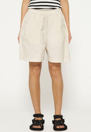 Beige katoenen shorts met een elastische tailleband, zijzakken en een relaxte fit, gecombineerd met zwarte sandalen met bandjes.