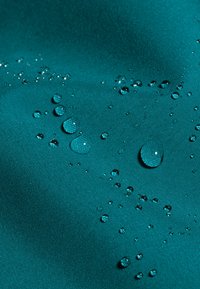 Gocce d'acqua di varie dimensioni su un tessuto liscio di colore turchese che mostra proprietà idrorepellenti.