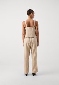 Combinaison beige avec un haut ajusté et des jambes amples. Présente des bretelles épaisses, une taille peplum flatteuse et une texture lisse et douce.