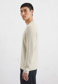 Crème-kleurige langetermijn gebreide shirt met een structureel patroon, ronde halslijn en aansluitend ontwerp, gecombineerd met donkere broeken.