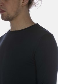 Schwarzes Langarmshirt mit gerippter Textur, Rundhalsausschnitt und tailliertem Design, seitlich gegen einen hellen Hintergrund gezeigt.