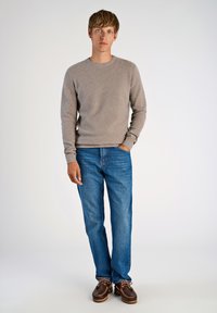 Suéter texturizado de color marrón claro, jeans de mezclilla azules y zapatos marrones. El suéter tiene cuello redondo y mangas largas, mientras que los jeans tienen un corte clásico.