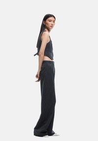 Ensemble deux pièces dénudé en gris foncé, comprenant un haut sans manches cropped avec un détail de nœud et un pantalon large taille haute.