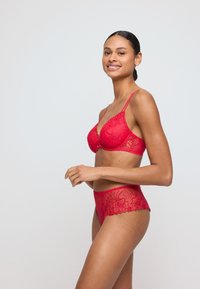Rode kanten lingerieset met een beugel-bh en bijpassende high-waisted slipjes, versierd met ingewikkelde bloemmotieven en gegolfde randen.