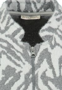 Sudadera de felpa gris y blanca con un patrón geométrico, que presenta un alto cuello, una textura suave y un cierre de cremallera de plástico. Etiqueta visible.