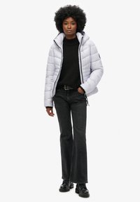 Ljusgrå puffjacka med huva, dragkedjestängning och kviltad design, kombinerad med en svart tröja, mörka jeans och svarta snörstövlar.