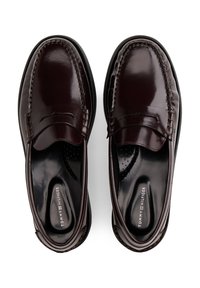 Sötét bordó bőrből készült mokaszinok varrott részletekkel, sima kivitelben, párnázott belső résszel, amely légáteresztő lyukasztásokat tartalmaz.