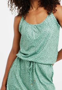 Débardeur vert menthe à pois noirs, en tissu doux, avec un col froncé et un cordon à la taille pour un ajustement réglable.