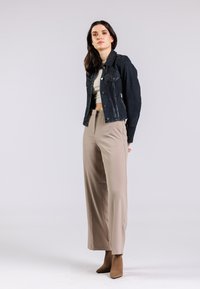 Giacca di jeans blu scuro con due tasche frontali, abbinata a pantaloni beige a gamba larga e stivali alla caviglia color cammello. Tessuti solidi, vestibilità su misura.