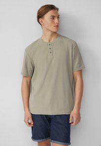 Korte mouwen, lichtgrijze henley-t-shirt in zachte stof met een ronde halslijn en een drieknoopsluiting. Draagt met donkere shorts.