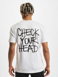 Fehér pamut póló rövid ujjakkal, a hátsó részén merész fekete graffitivel "CHECK YOUR HEAD" felirattal. Simább textúra.