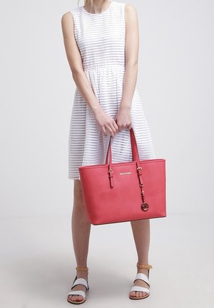 Rosa faux lederen totebag met dubbele handvatten, metalen hardware en een decoratieve sleutelhanger; gecombineerd met een wit gestreept jurk en sandalen.