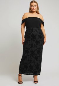 Svart off-shoulder maxiklänning med en figurnära bodice och en flödande kjol, med texturerade blomsterdesigns och mjukt tyg. Svarta remsandaler.