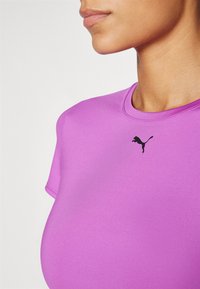 Lilla spordisärk, mis on valmistatud elastsetest materjalidest, ümarate kraega ja musta Puma logoga rinnal. Sile tekstuur.