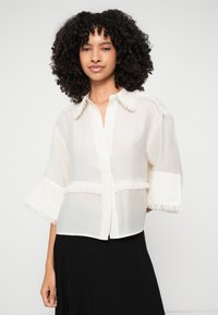 White, short-sleeve shirt with a fringed collar and hem. Made of lightweight fabric, featuring a button-down front and a relaxed fit.