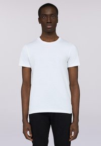 Bílá bavlněná tričko s kulatým výstřihem, krátkými rukávy a decentním logem na levé hrudi. V kombinaci s černými džíny.