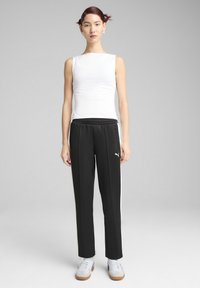 Biała bezrękawnik zestawiona z czarnymi spodniami sportowymi z białymi paskami po bokach i kieszeniami na zamek, uzupełniona o casualowe sneakersy.