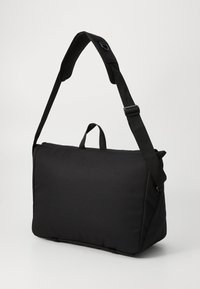 Sac messager noir en tissu durable, avec une forme plate, une bandoulière réglable, une poignée supérieure et une texture lisse au design minimal.
