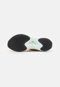 Semelle d'une chaussure de course Nike montrant un motif texturé noir sur l'avant-pied et le talon, une semelle intermédiaire blanche et un swoosh Nike vert visible à travers une découpe.