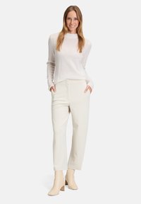 Jasno beżowe dopasowane spodnie z bocznymi kieszeniami, w połączeniu z miękkim, jasnoszarym swetrem z długim rękawem i kremowymi botkami za kostkę. Gładka tekstura.