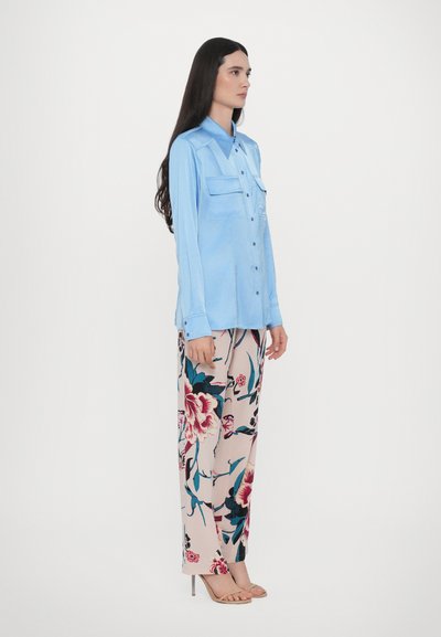Cămașă bleu deschis, cu două buzunare pe piept, asociată cu pantaloni largi cu un model floral în nuanțe de bej, roz și teal. Textură fină.