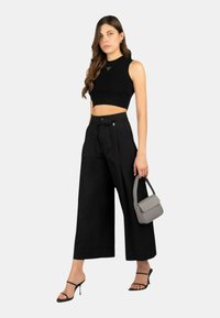 Top cropped nero, pantaloni neri a gamba larga, tacchi neri con cinturini e una piccola borsa grigia con chiusura a patta. La modella indossa l'outfit.