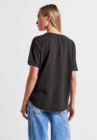 Maglietta nera a maniche corte con un motivo geometrico testurizzato, collo rotondo, vestibilità rilassata e orlo dritto, abbinata a jeans azzurri chiari.
