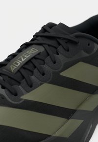 Čierne atletické topánky s štruktúrovaným zvrškom, zelenými pruhmi a logom "ADIZERO." Ľahká konštrukcia s zaoblenou špičkou.