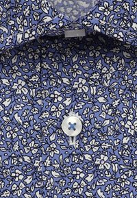 Tessuto della camicia floreale blu con motivi di fiori e foglie bianche, caratterizzato da un bottone con un design a croce blu. Tessuto texture e dettagli del colletto visibili.