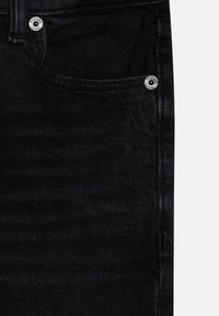 Tessuto denim nero con una texture liscia, dotato di una tasca frontale e dettagli in metallo argentato sui bottoni.