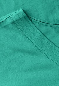 Turquoise katoenen stof met een v-hals ontwerp, met een gladde textuur en nette, contrasterende stiksels langs de halslijn.