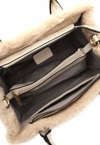 Beige handbag with a textured, fluffy exterior. Interior features multiple compartments, including one zipped pocket and gold-tone hardware.