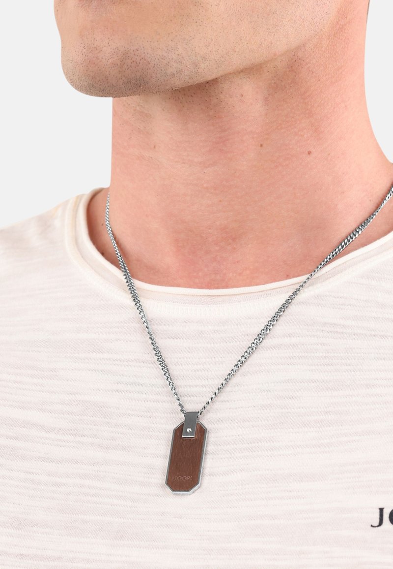 Collana in argento con un ciondolo rettangolare caratterizzato da un'intarsio in legno e accenti in argento, indossata sopra una maglietta leggera e testurizzata.
