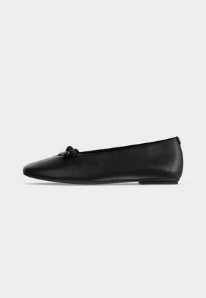 Ballerine noire en cuir avec un petit nœud sur le devant et un petit talon, vue de profil sur fond blanc.