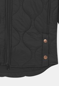 Chaqueta acolchada negra con un patrón de olas, que cuenta con una cremallera de longitud completa y botones a presión de color cobre en el dobladillo. Textura suave.