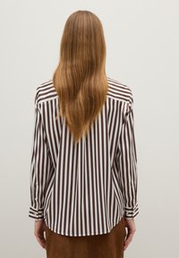 Person with long light brown hair wearing a vertically striped brown and white long-sleeve shirt, shown from the back against a plain background.