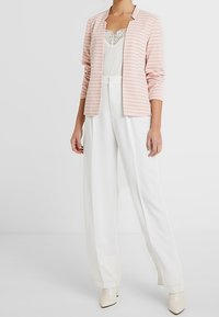 Rosa stribet blazer over en hvid blonde cami og hvide vide bukser. Sættet har glatte teksturer og figursyede designs.