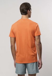 Oranžové bavlnené tričko s krátkym rukávom, s okrúhlym výstrihom a hladkou textúrou, v kombinácii s pruhovanými zelenými šortkami.