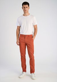 Czerwone bawełniane spodnie w wąskim kroju, z zamkiem błyskawicznym i zapięciem na guzik, zestawione z gładką białą koszulką z krótkim rękawem oraz białymi trampkami.