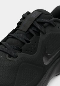 Gros plan sur une chaussure de course Nike noire avec un tissu texturé, des lacets à motifs et une étiquette "Run Stronger" sur la languette.
