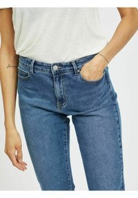 Jeans de ganga azuis de cintura alta com cinco bolsos, passadores de cinto e fecho com botão na frente. O tecido tem um acabamento suave e ligeiramente texturizado.