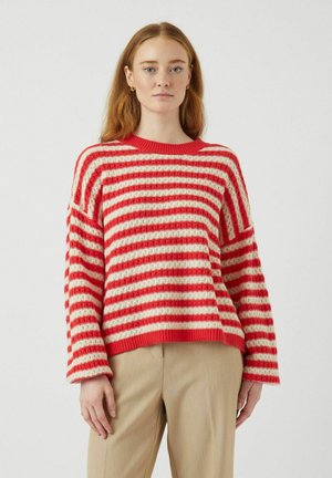 Gestreifter Pullover in Rot und Creme, lockere Passform, gestrickte Textur, runder Halsausschnitt, überschnittene Schultern, kombiniert mit beigen Hosen.