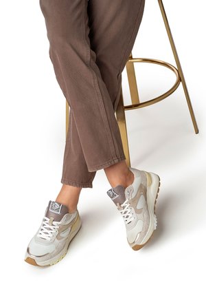 Baskets blanches et grises avec accents en mesh, semelle en caoutchouc, détails texturés et bout rond, associées à un pantalon en velours côtelé marron.