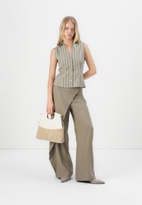 Gestreifte ärmellose Bluse in Beige und Grün, kombiniert mit olivfarbenen weiten Hosen. Accessoires sind eine cremefarbene Tasche mit strukturiertem Boden.