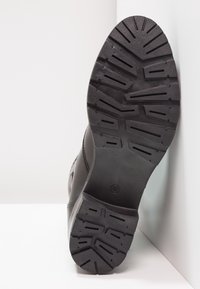 Svart gummistövelfot med en texturerad, mönstrad yta. Rund tå och kraftiga kanter, med storleksmärkning "37" präglad nära hälen.