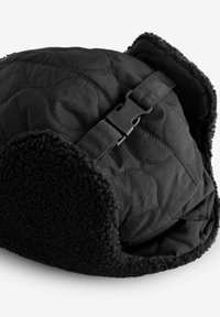 Must have mustriini, pehmea shearlingi äärisega. Omab külgklambrit reguleerimiseks ja tekstuurilisi mustreid väliskangas.