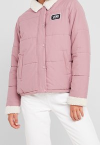 Lyserød pufferjakke med sherpa krave, udstyret med et quiltet design og trykknapper; to sidelommer; brandlogo på brystet.