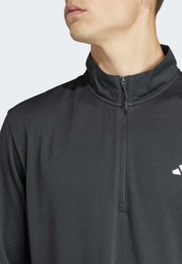 Schwarzes, langärmliges Zip-Up-Oberteil aus glattem Stoff. Hoher Kragen und kleines weißes Logodetail im Brustbereich.