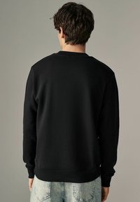 Sudadera de forro polar negra con cuello redondo, mangas largas y puños acanalados, combinada con jeans de mezclilla de color azul claro.