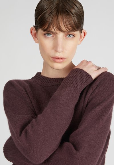 Un maglione a coste bordeaux con scollo rotondo e maniche lunghe, caratterizzato da una texture morbida e un calore discreto.
